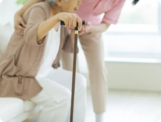 杖をついて歩く高齢女性を支えるスタッフ